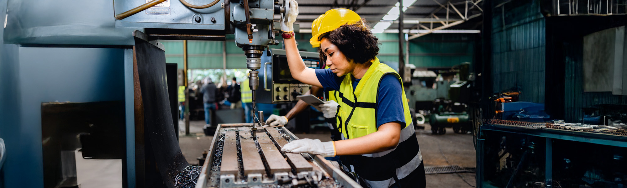 Women workers or mechanics in safety uniforms are working on metal drilling machines